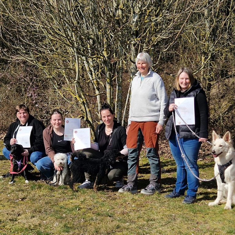 Gruppierung von Personen mit Hunden im Freien, alle halten Urkunden in den Händen.