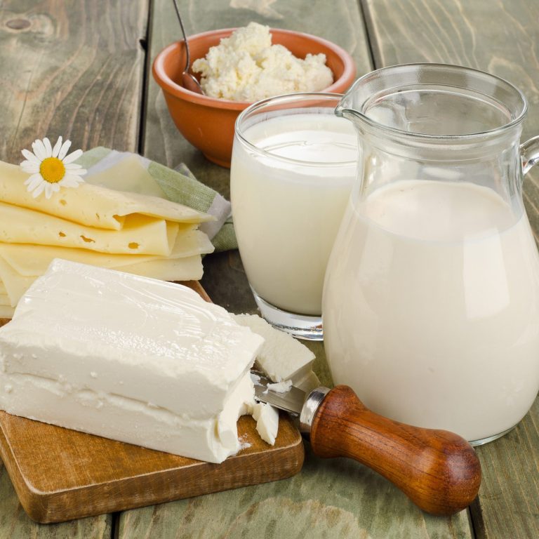 Käse, Joghurt, Milch und Quark auf einem Holzbrett mit einem Blumenmotiv.